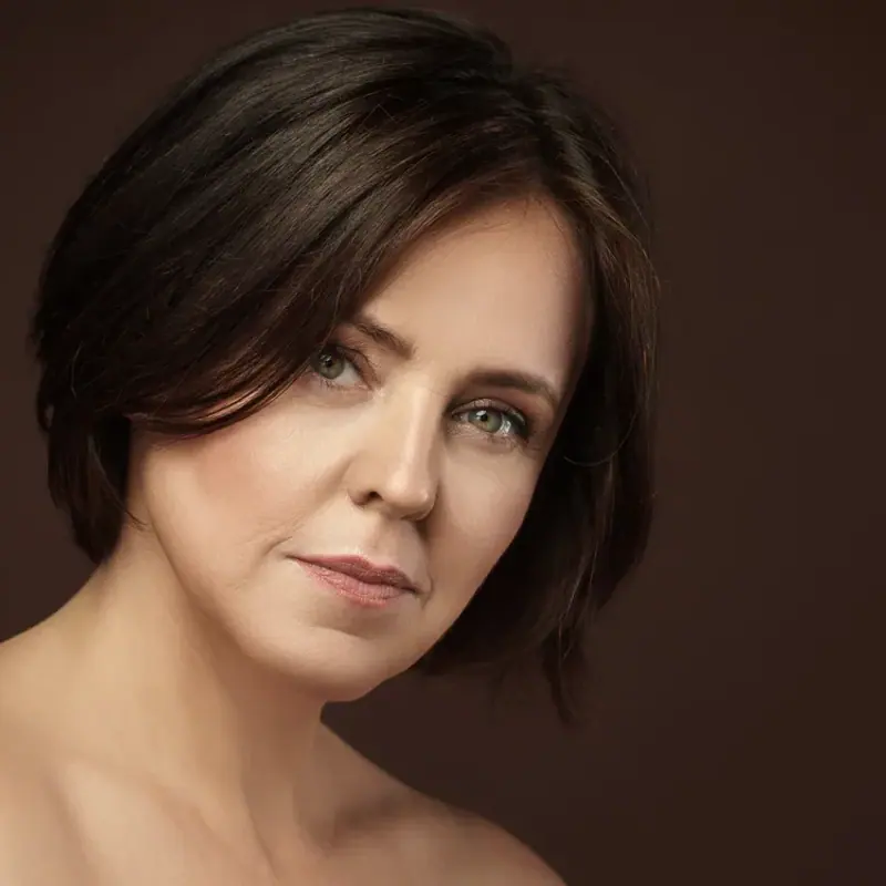 A woman with a dark bob photographed against a warm brown backdrop in soft studio light
