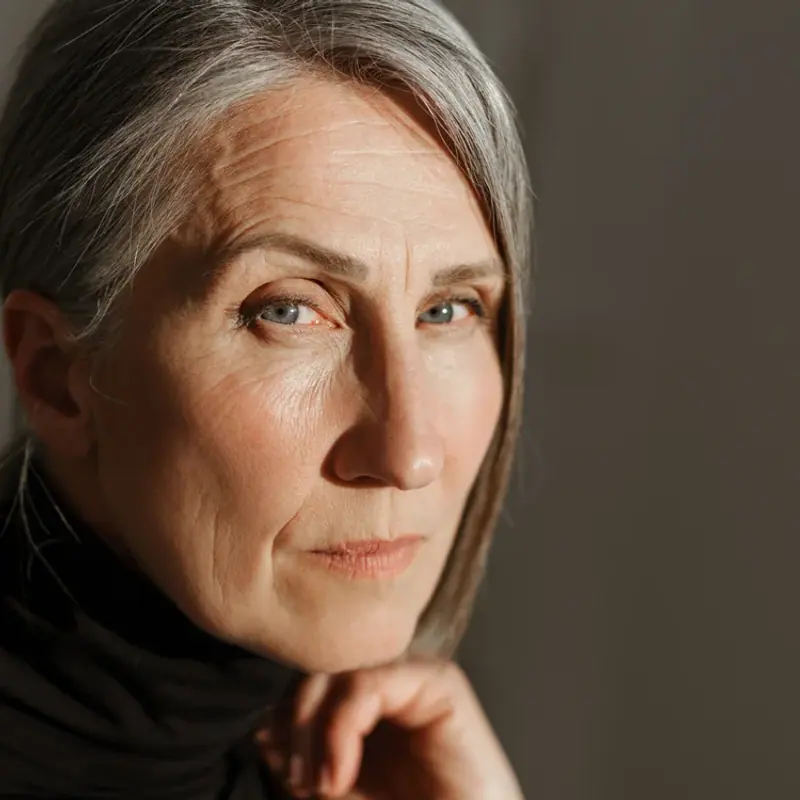 A woman with grey hair in a black turtleneck, photographed in soft indoor light