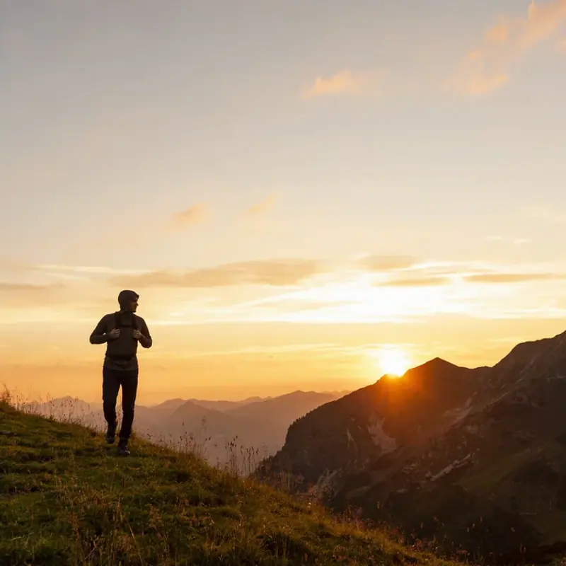 A lone figure moving along a mountain ridge at sunrise