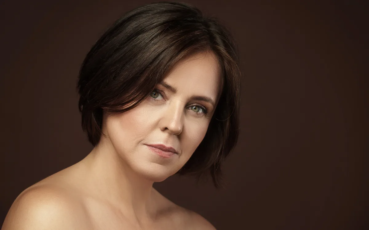 A woman with a dark bob photographed against a warm brown backdrop in soft studio light