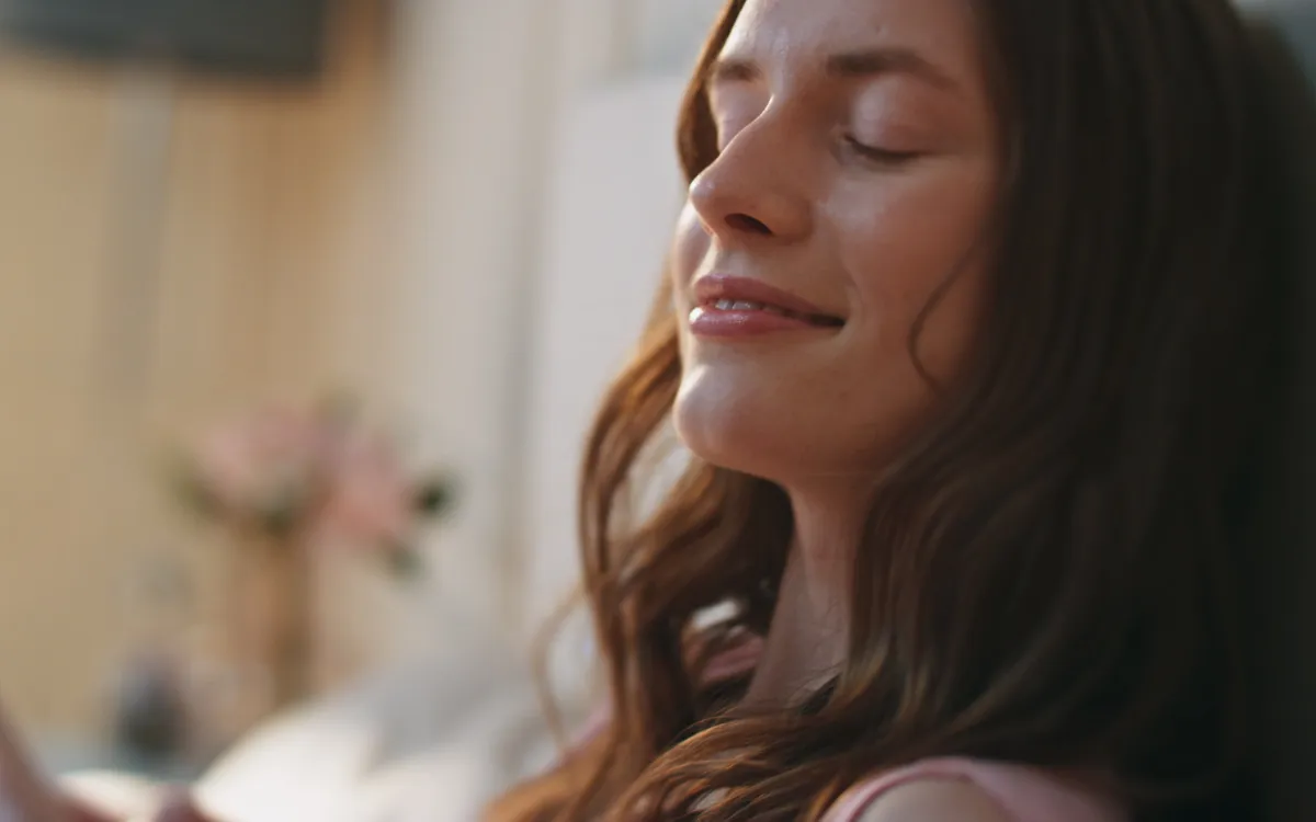 A woman with long brown hair resting with her eyes closed in soft indoor light