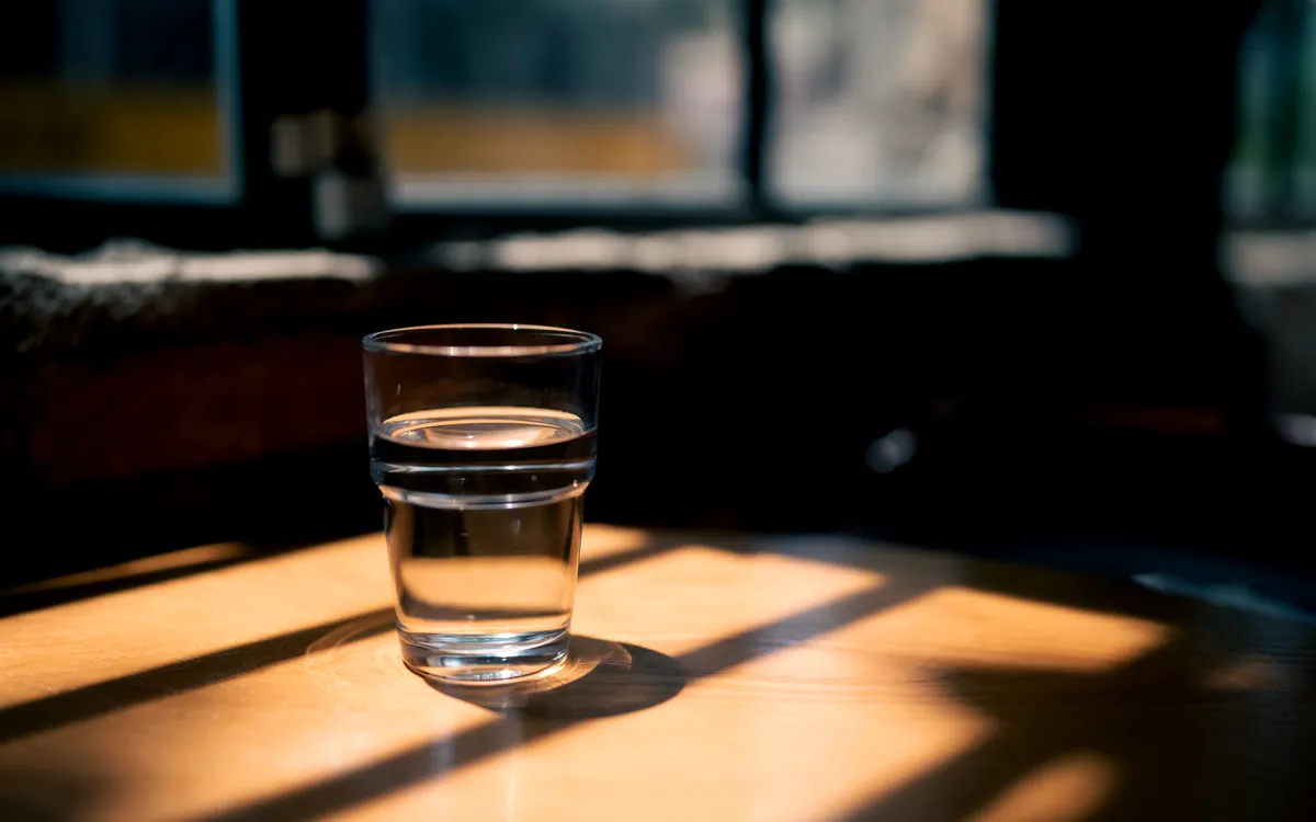 A glass of water on a wooden table in a shaft of warm, low sunlight