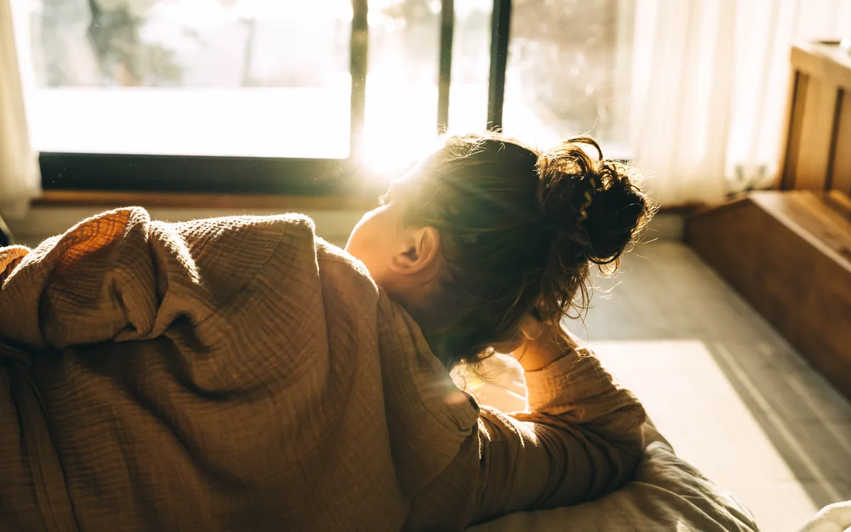 A woman resting her head on her arms in bed, backlit by low morning sun