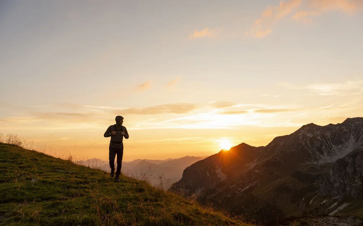 A lone figure moving along a mountain ridge at sunrise